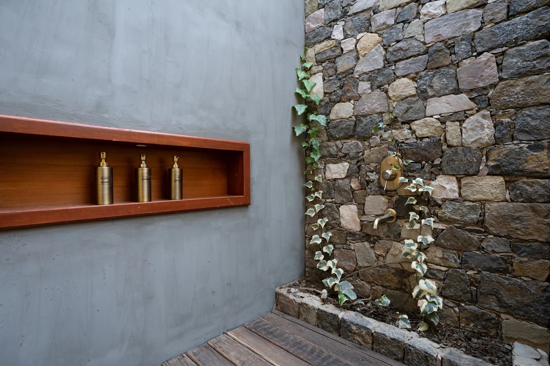Outdoor stone shower with copper basin and ivy growing over the wall at Kaansya