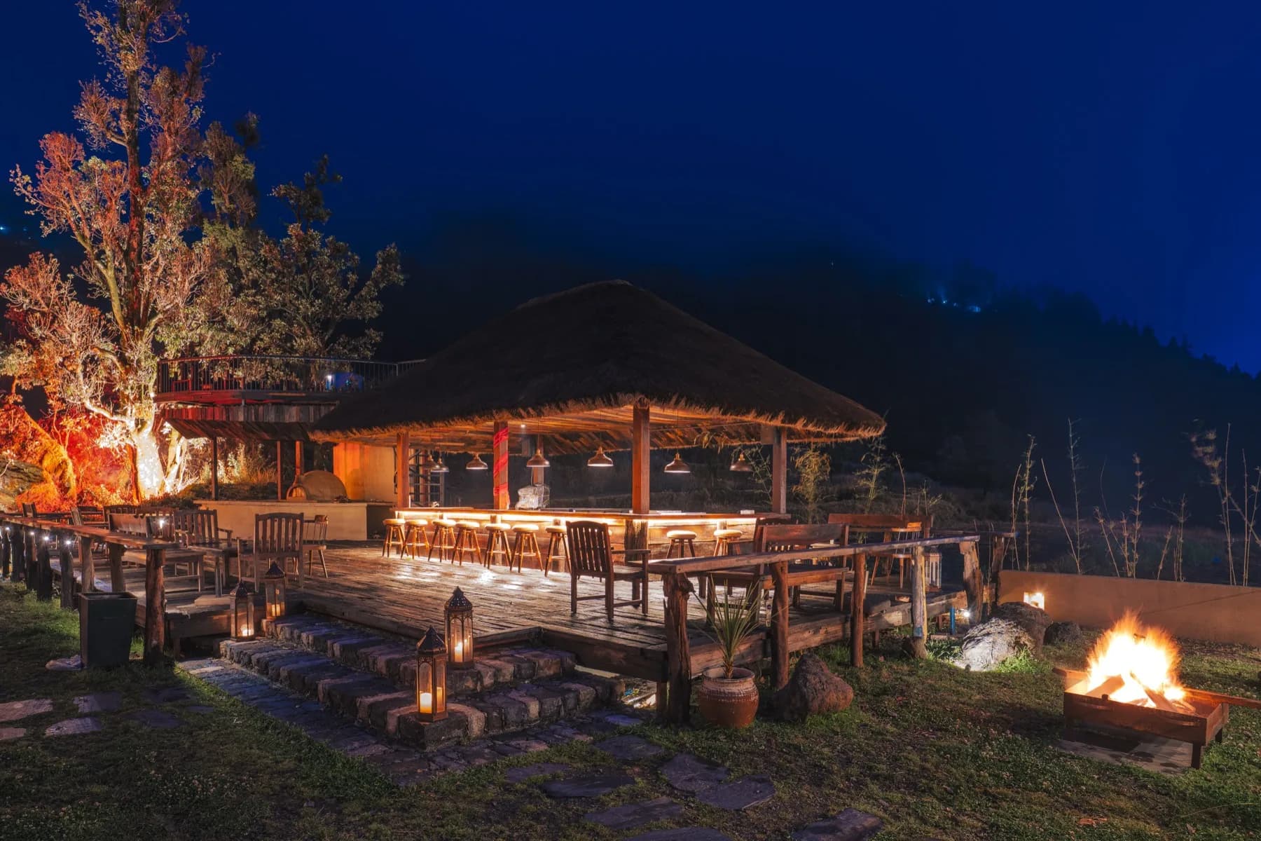 Open-air bar at Kaansya glowing with amber lanterns and a small bonfire under the night sky
